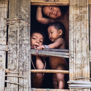 Kids from the Mru tribe in rural Bangladesh peeking out of their bamboo hut…