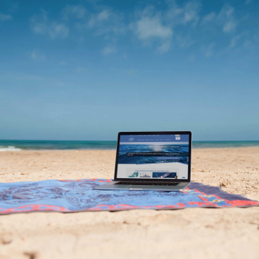 A peaceful beach setting with a laptop, illustrating the essence of slow travel and oceanic exploration in today's fast era.